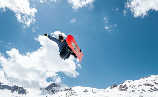 Snowboarder springt vor Bergkulisse mit Schnee und blauem Himmel