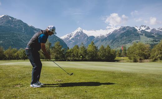 Golfer schlägt Ball auf Grün vor Bergpanorama